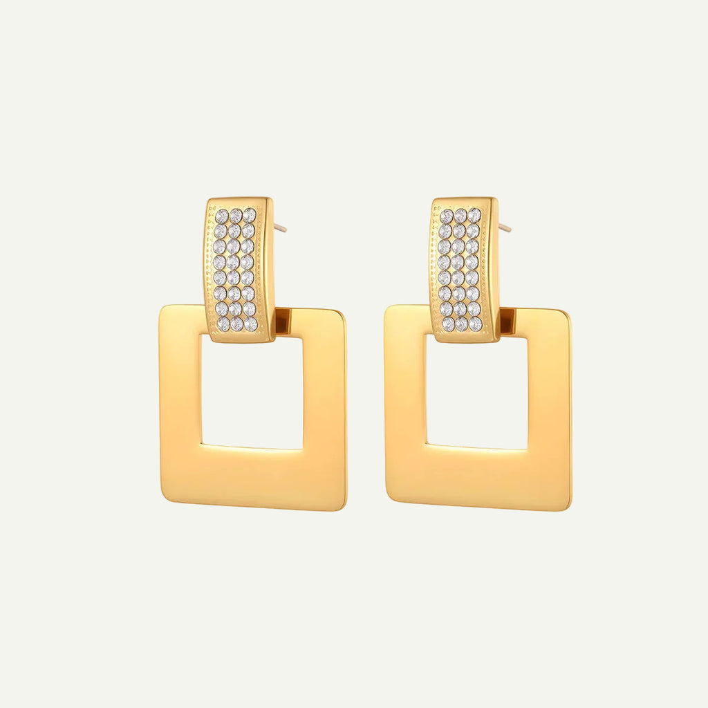 Gold square earrings with clear gemstones on a beige background