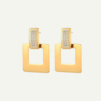 Gold square earrings with clear gemstones on a beige background